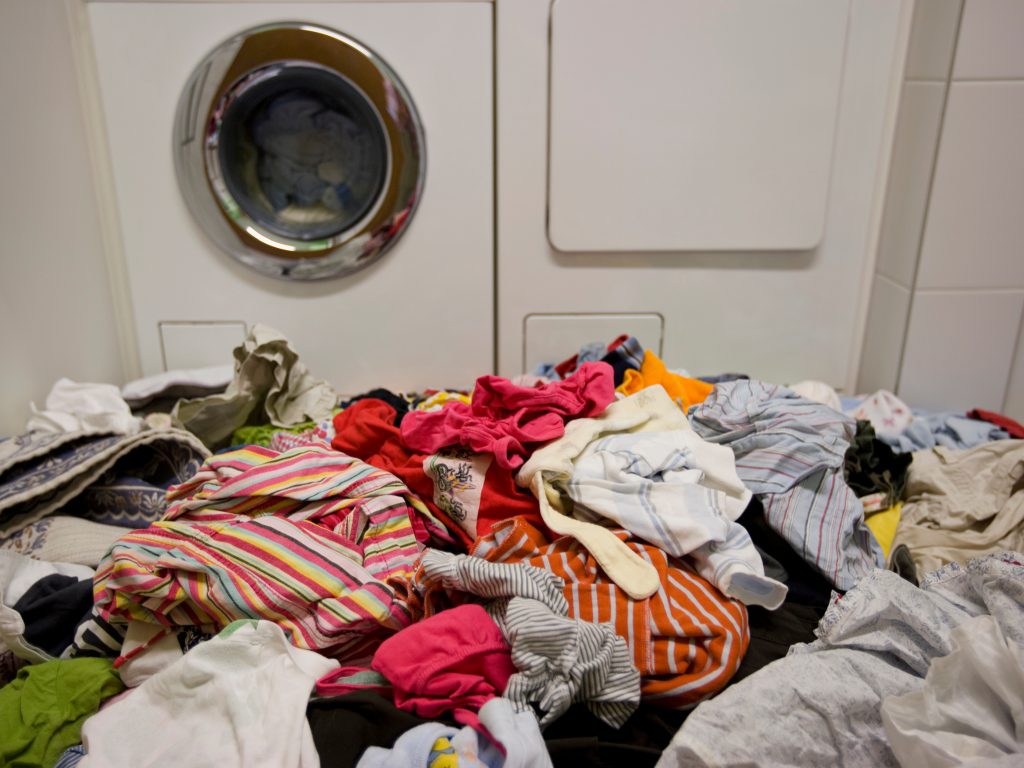 A pile of laundry in front of a broken washing machine